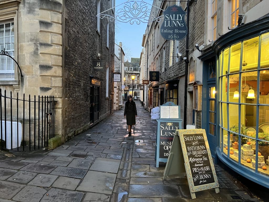  Weekend Guide to Bath: Bejal wearing a khaki winter coat and faux fur hat with boots walking past Sally Lunns Eating House, bath