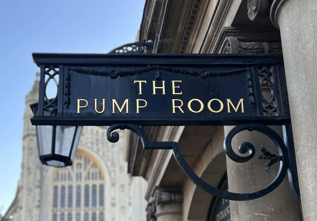 The Pump Room Bath black sign with gold lettering against the backdrop of Bath Abbey