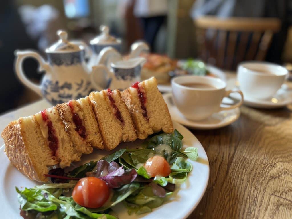 Vegetarian restaurants in Bath. A brie and cranberry bun cut into small triangles at Sally Lunn's Eating House. The gun is on a white plate with a dressed mixed leaf salad with baby tomatoes. There is a blue and white China tea pot and white tea cups in the background.