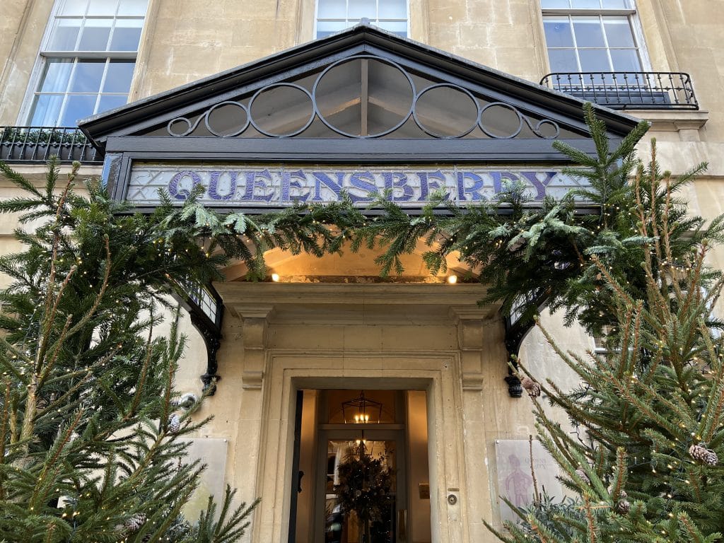 The Queensberry Hotel, Bath, exterior door that reads, Queensberry  in dark blue. The doorway is decorated with ever green foliage for Christmas