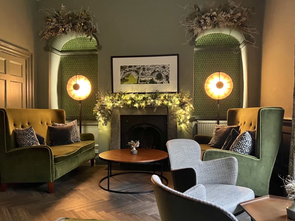 The Queensberry Hotel lounges. This one is decorate din sage green with studded velvet sofas and comfy chairs around a fireplace. The Fireplace is decorated with pretty Christmas decorations at the Queensberry Hotel: a luxury boutique hotel in Bath