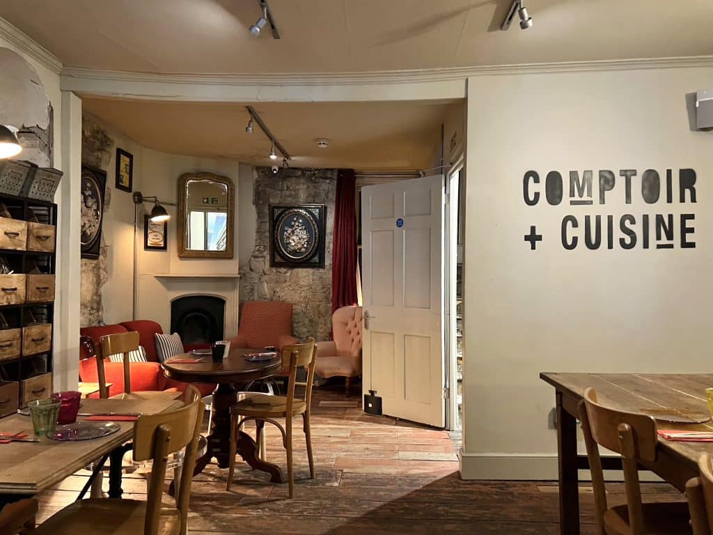 Interiors at Comptoir + Cuisine in Bath. Wooden mismatched chairs and bistro style tables with shabby chic mirrors and colourful upholstered chairs in the upstairs space.