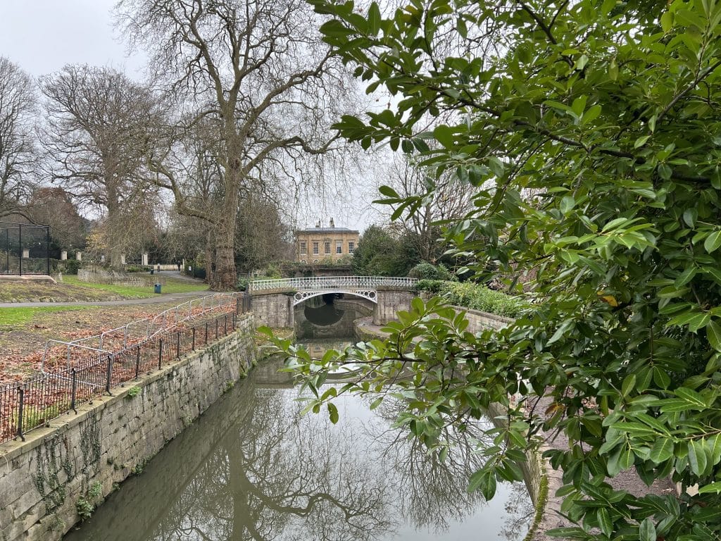 The Sydney Gardens bridge with plants and bushes framing the image in Bath. The River is running through under the bridge