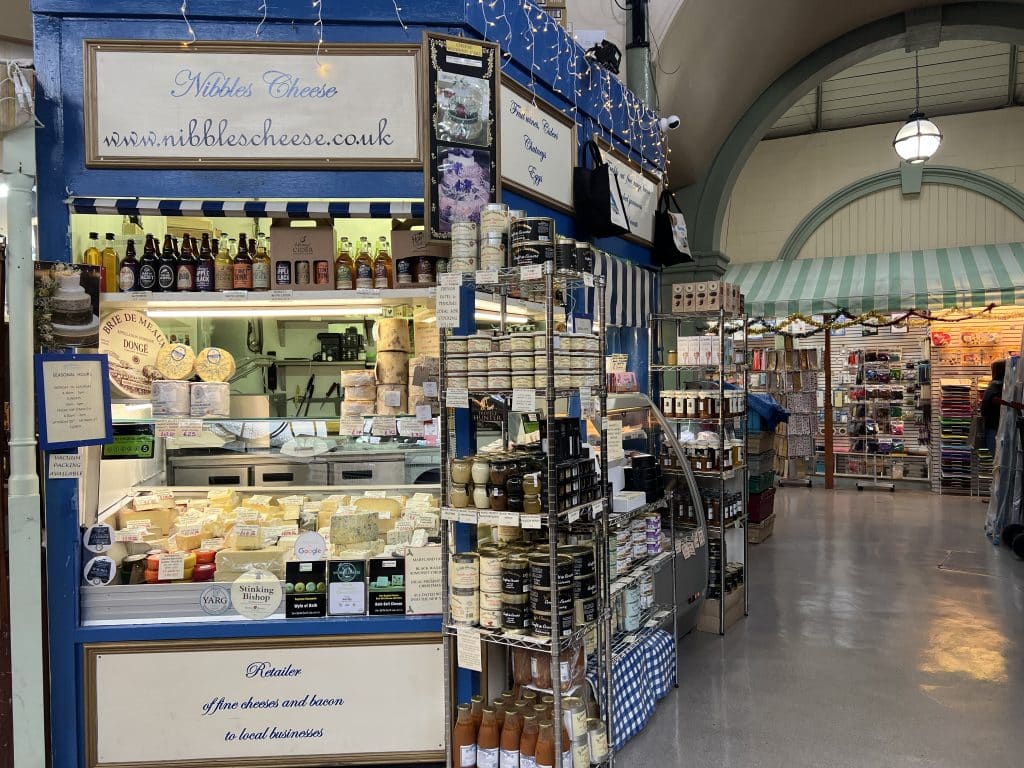 Blue Nibbles Cheese stall in Bath inside the Guildhall Market. There are lots of cheese and chutneys piled outside the stall