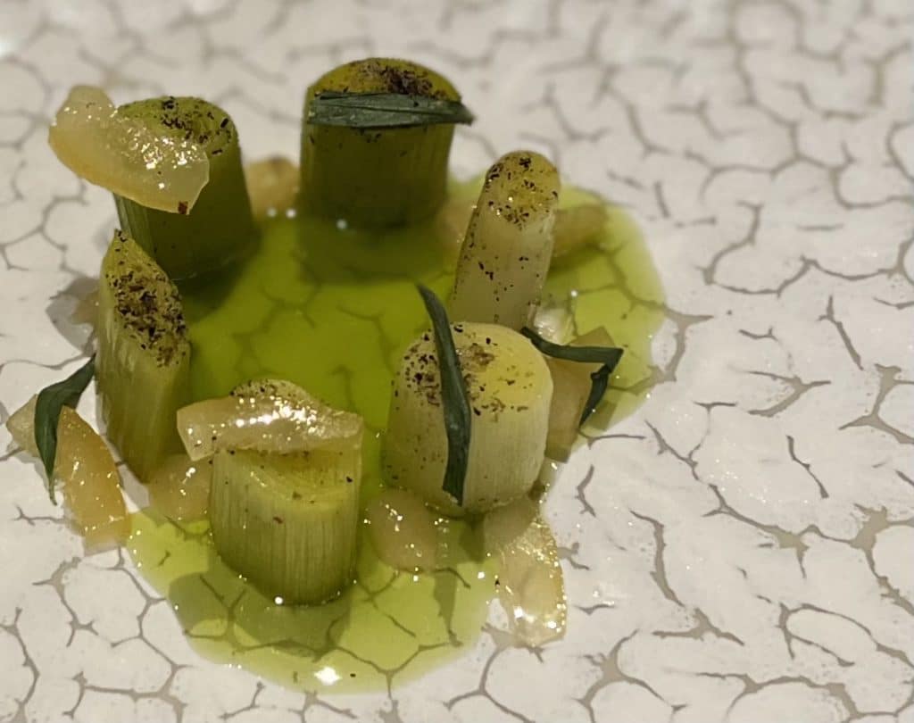 Leeks medley dish at  Olive Tree at Queensberry Hotel in Bath. The leeks are served on a light green jus on a marble effect white and grey plate.