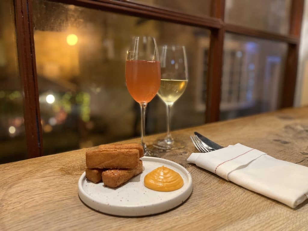 Potato croquettes mall plates at Oak Restaurant Bath. There are two glasses of ornage and white wine with cutlery and a napkin, looking out across the street