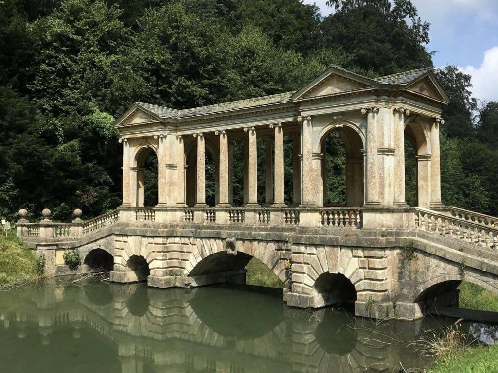 The Palladian Bridge at Prior park surrounded by trees and a river running under it in Bath