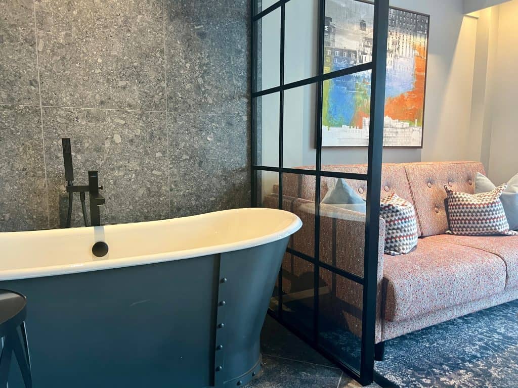 Hotel Brooklyn modern grey roll-top bath in room with a screen partition and sofa