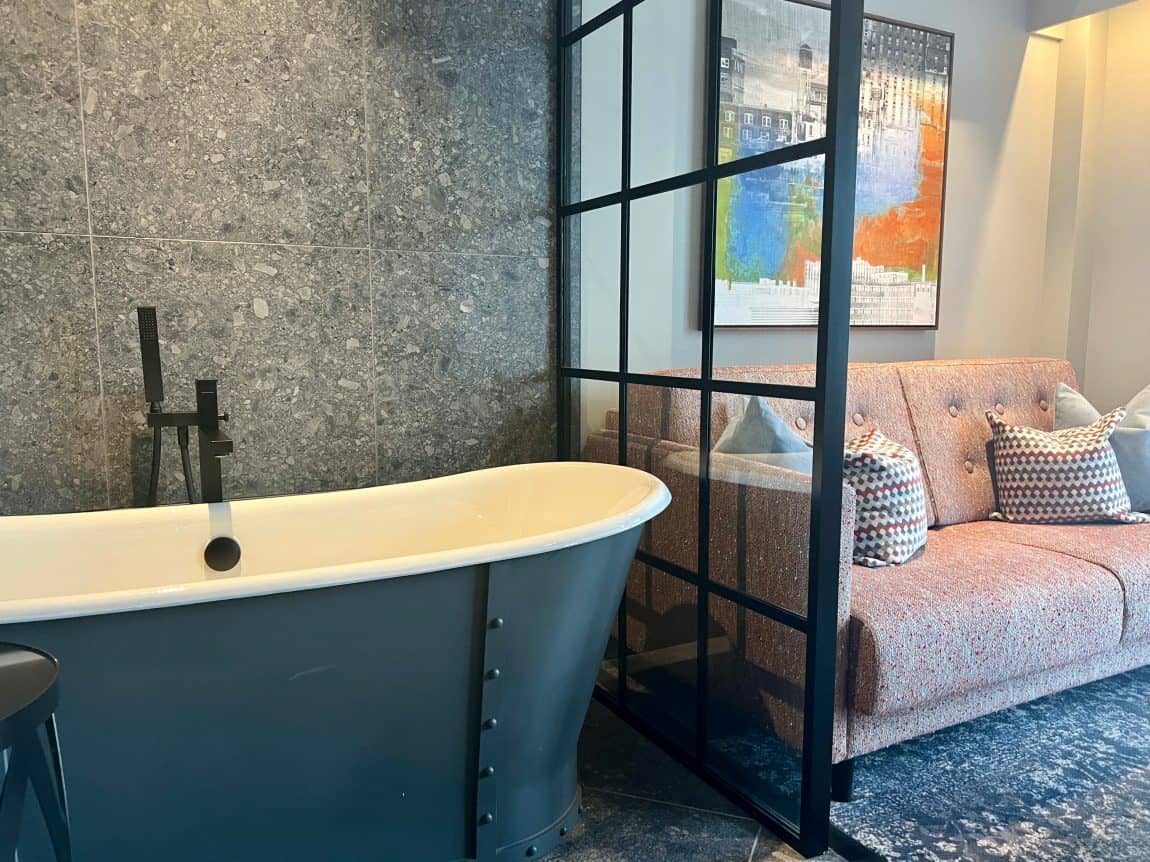 Hotel Brooklyn modern grey roll-top bath in room with a screen partition and sofa