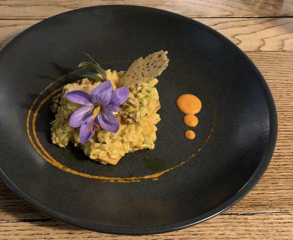 Vegetarian Food in Scotland, East Haugh House. A black plate with Butternut squash, sage and roast walnut risotto on it topped with edible flowers.
