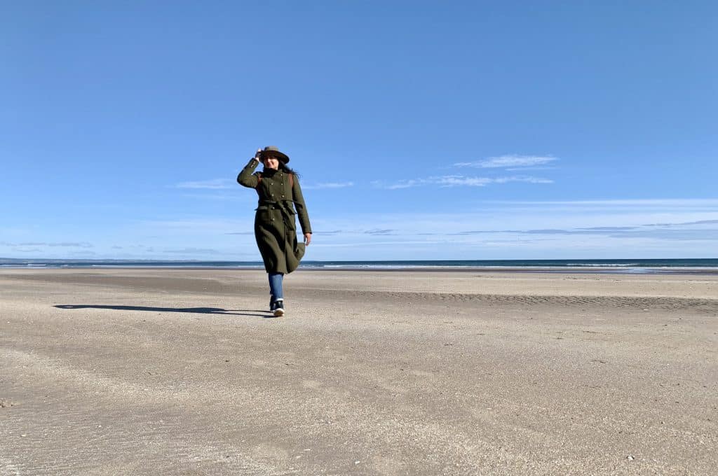 Villages and towns in Fife: West Sands Beach, St Andrews, Fife with Bejal walking down beach in a khaki coat and hat