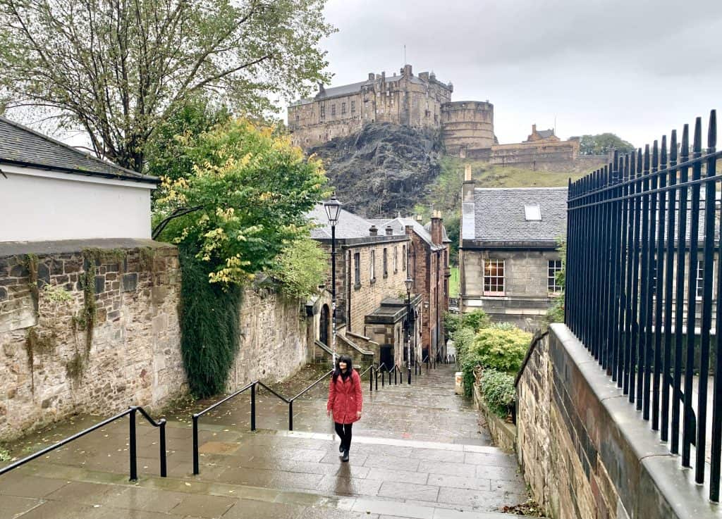 one of the Photo Locations in Edinburgh with Bejal wearing a red coat walking up the Vennel. Views of Edinburgh Castle in the background