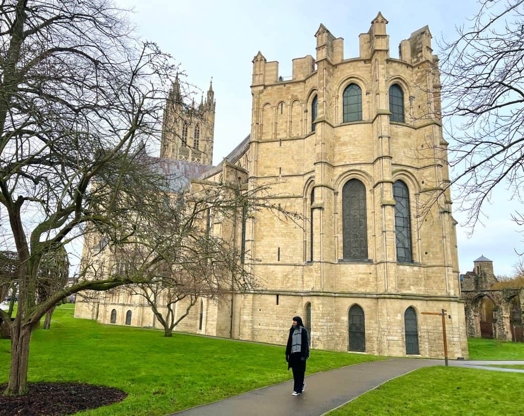 The best of Canterbury, Canterbury Cathedral Rear Exterior with Bejal standing outside. Green grass and a bare tree in front.