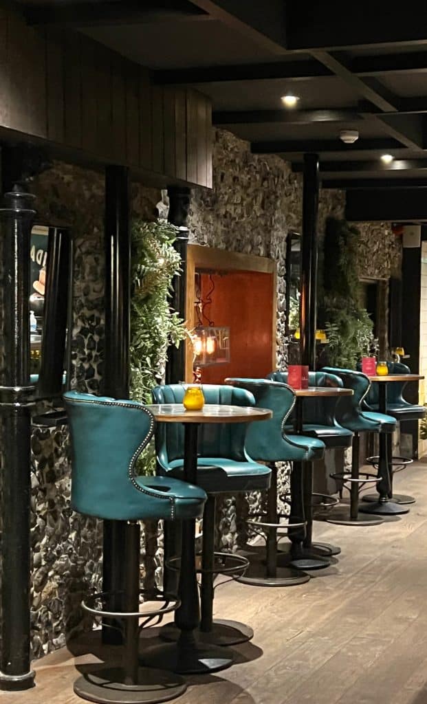 The Falstaff, Canterbury: bar with teal bar stools and tables with small tea light containers. There are plants in pots up the wallls