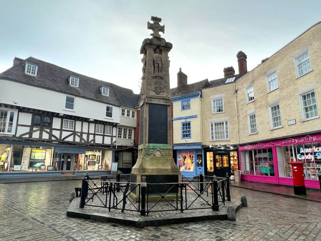 The best of Canterbury must-visit, The Canterbury War Memorial with colourful shop fronts in the background and a fence around teh memorial itself on a cloudy day