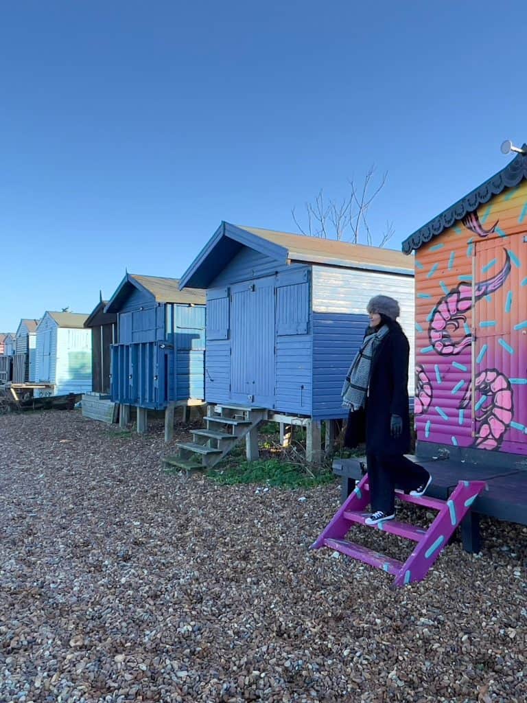 Beach huts on Tankerton Beach, Whitstable, with Bejal down the stairs in a black coat and Russian-style hat.