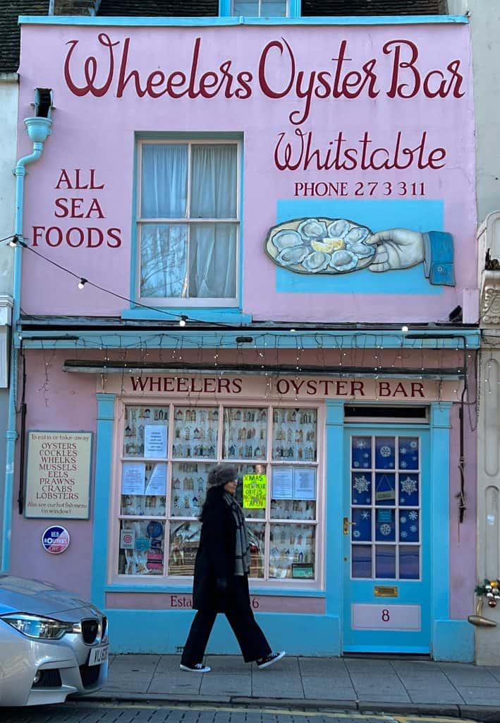 Whitstable Oyster Company Pink Exterior with Bejal walking past outside and a car front peeking into the image