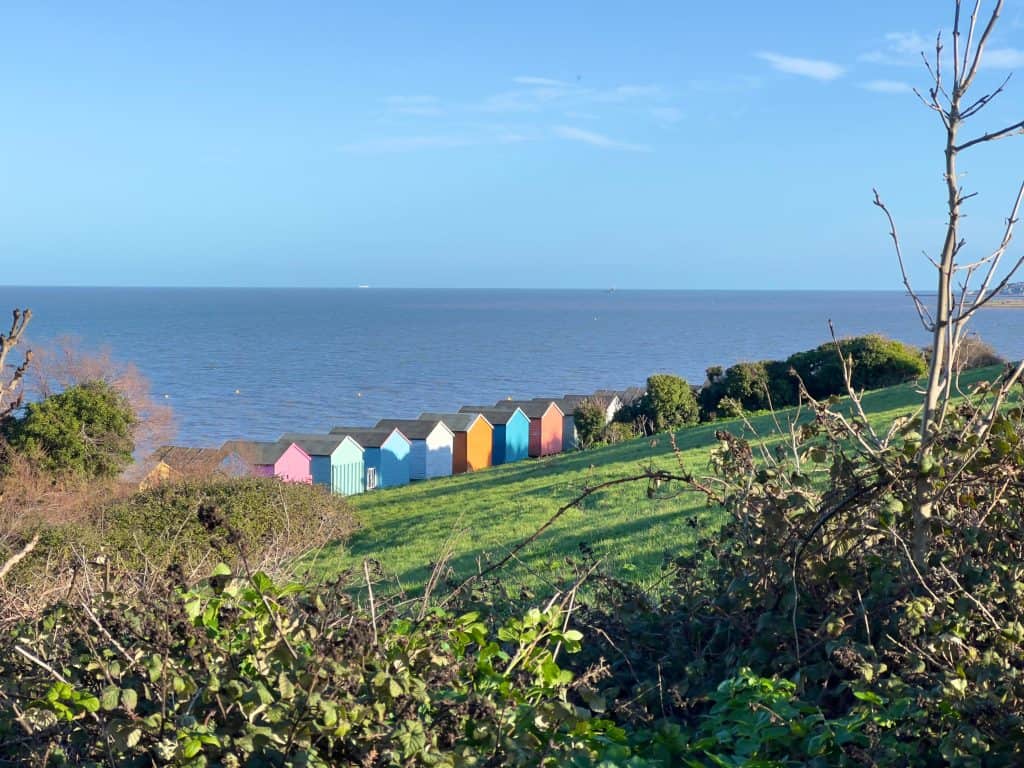 Herne Bay multicolour beach huts facing the sea with blue skies and folidage around the sides