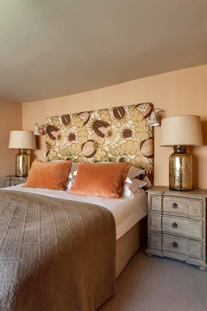 Superior Bed Room at The Falstaff in Canterbury, The headboard it drown and white with pale orange scatter cusions and a grey throw. There are two silver lamps at eitehr sid eof the bed. 