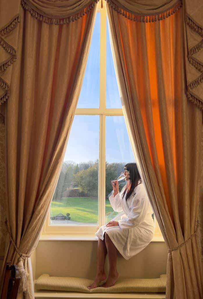 Bejal drinking champagne in bath robe in Baker Street window seat