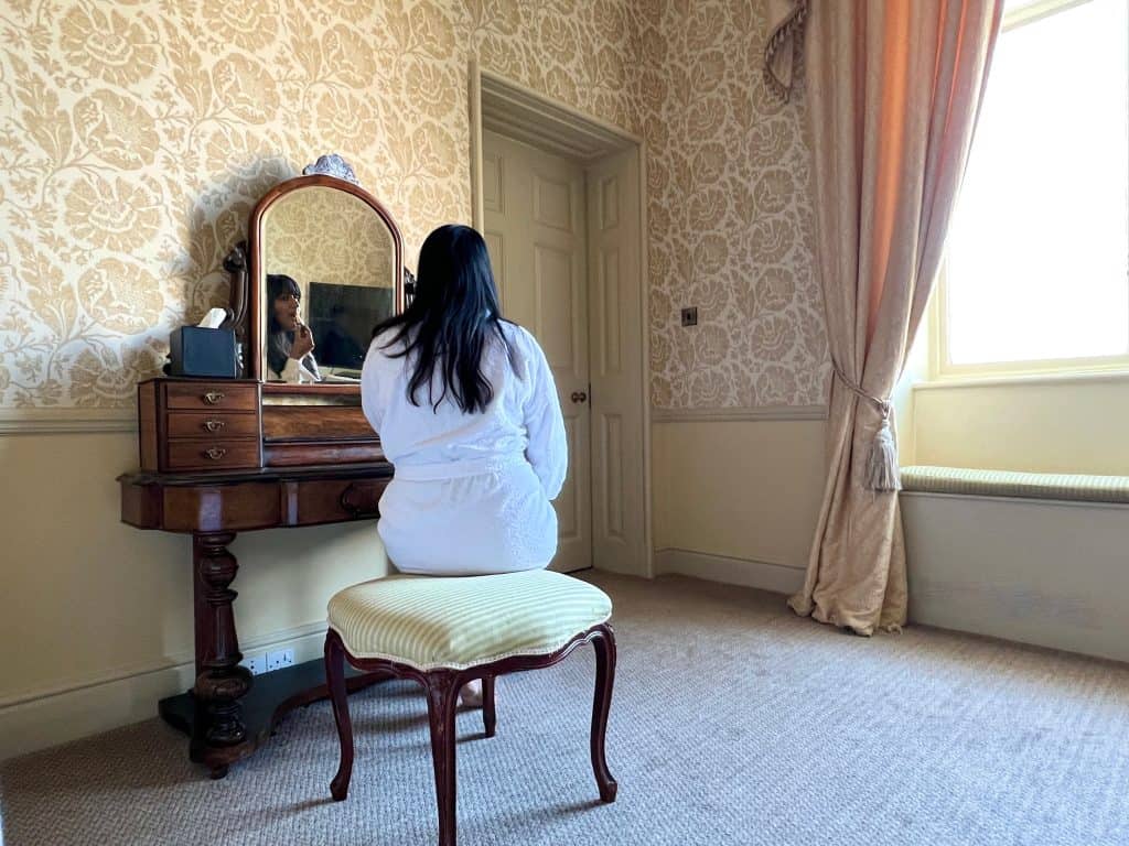 Bejal sitting in bathrobe at dressing table in Baker Suite