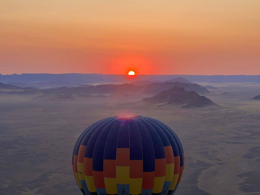 Sunrise in hot air balloon with top of another hot air balloon in front