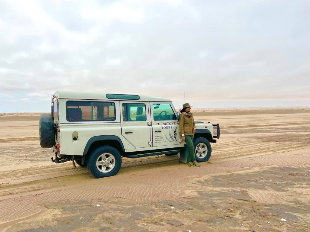 Bejal standing in front of Touchstone Tours safari truck on Garnet Beach