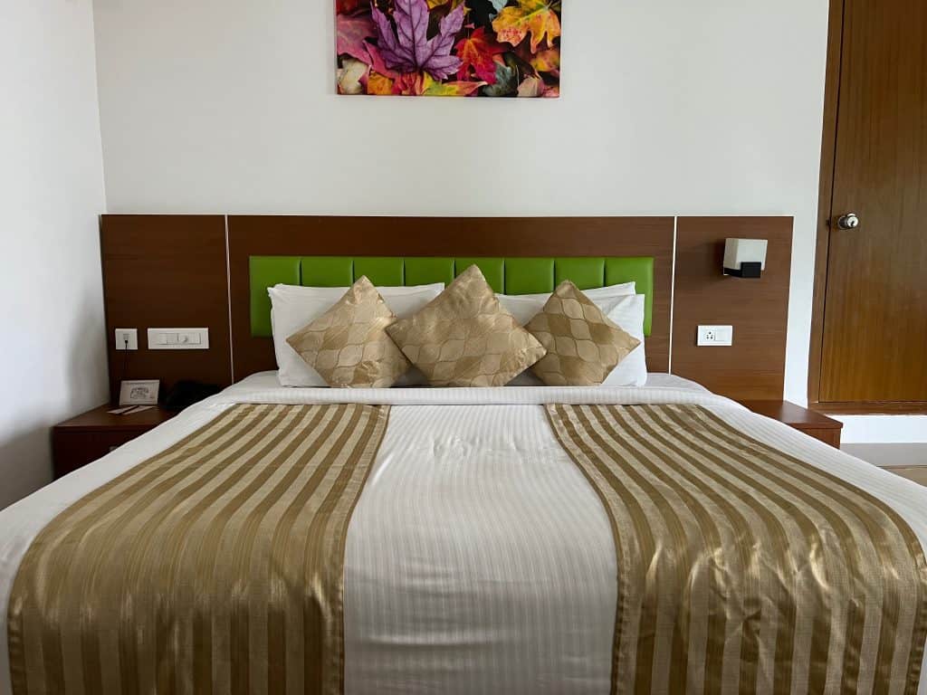Eco-friendly Hotels in Kerala: Double bed at Green Leaf Resort covered with a gold bed spread and co-ordinating scatter cusions.