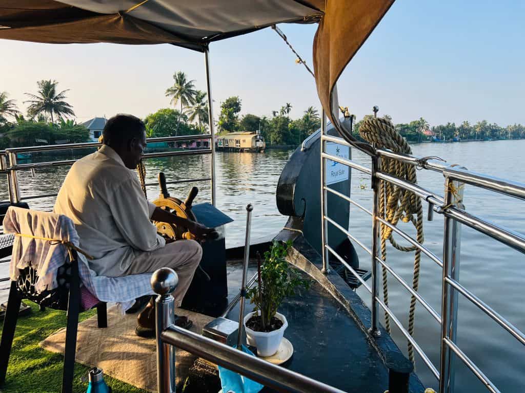 Eco-friendly hotels in Kerala: captain steering luxury Royal Suite houseboat