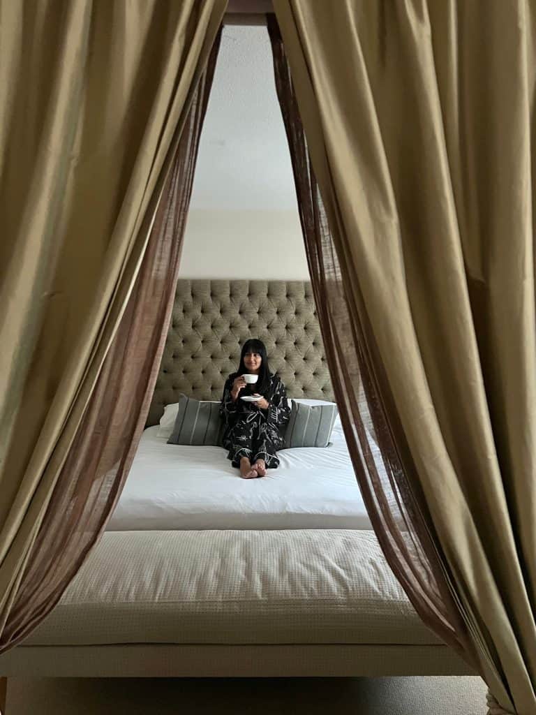 Bejal sat on middle of bed with cup of coffee