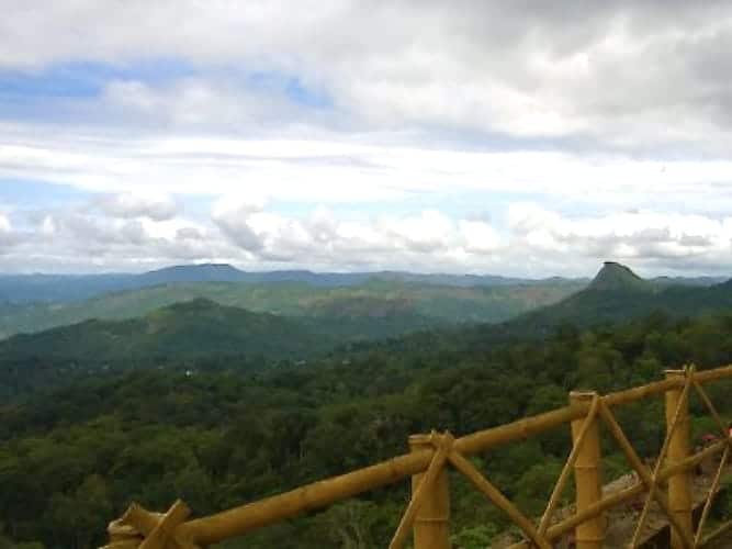 The Karadipara View Point with low clouds adn lush green hills wit a brown wooden fence
