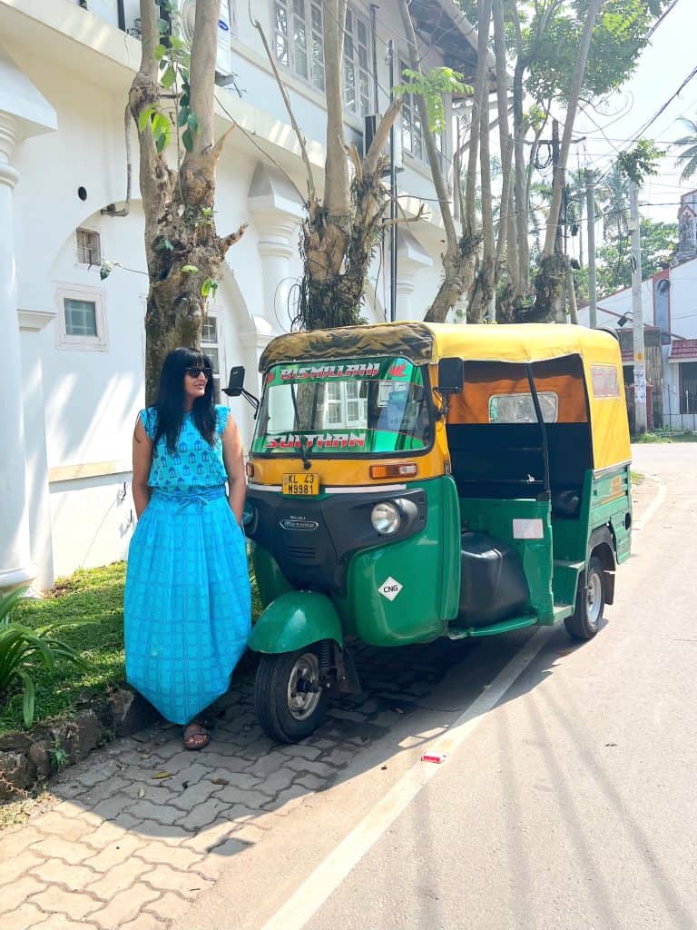 Bejal wearing a turquoise skirt and top standing next to a dark greena dn yellow rickshaw in Fort Kochi