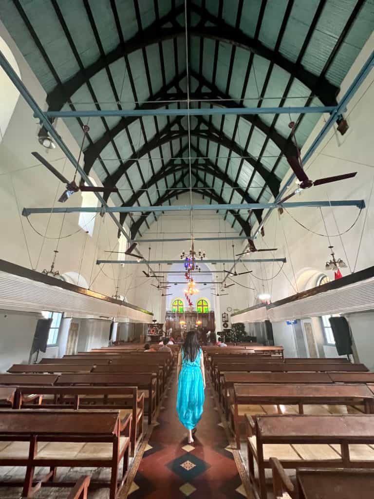 48 hours in Fort Kochi. Bejal walking down the centre aisle of St Francis Church. Ther are dark brown wood pews on either side, with the alter at the end of the church right ahead.