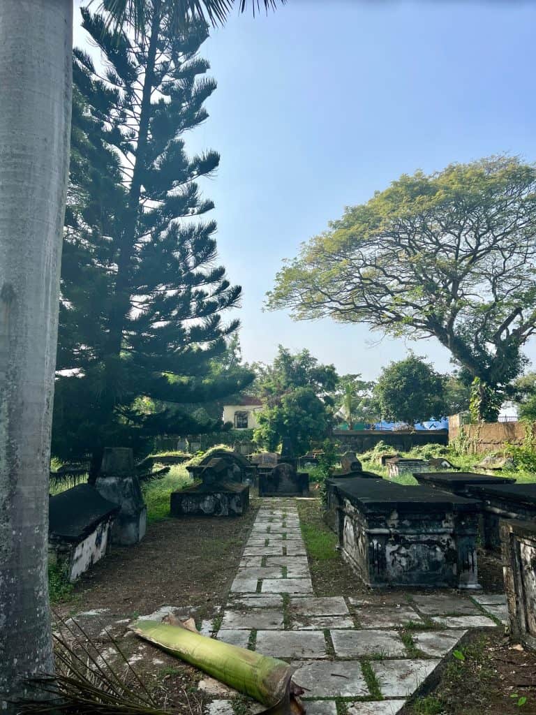 Tombs inside the Dutch Cemetery with tall green trees surrounding the graves