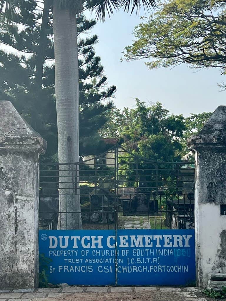 48 hours in Fort Kochi. The Dutch cemetery sign from outside and locked gates. In the distance tombs can be seen.