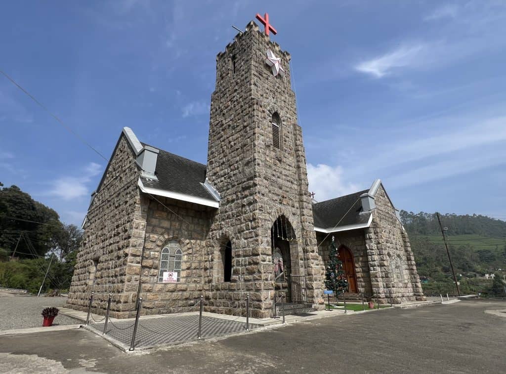 The exterior of the oldest church in Munnar, Christ Church. theer are hills and trees in the distance.