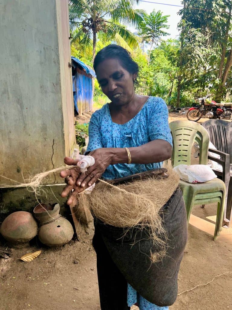 Local lady making coir string during a visit to Back @ village: Showing why Kerala is one of India's friendly states. Lady wearing blue top twisting coir thread between her fingers to make a thicker rope like structure.