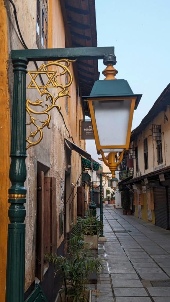 The main jew Town street with one of the pretty green and yellow lamp and benches in the background. The street has yellow and brown painted buildings.