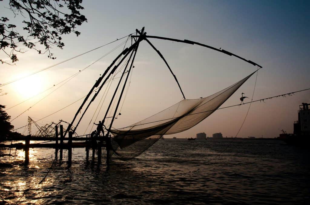 48 hours in Fort Kochi. Fort Kochi fishing nets at sunset. Dimly lit photo with a pink/purple sky in the background.