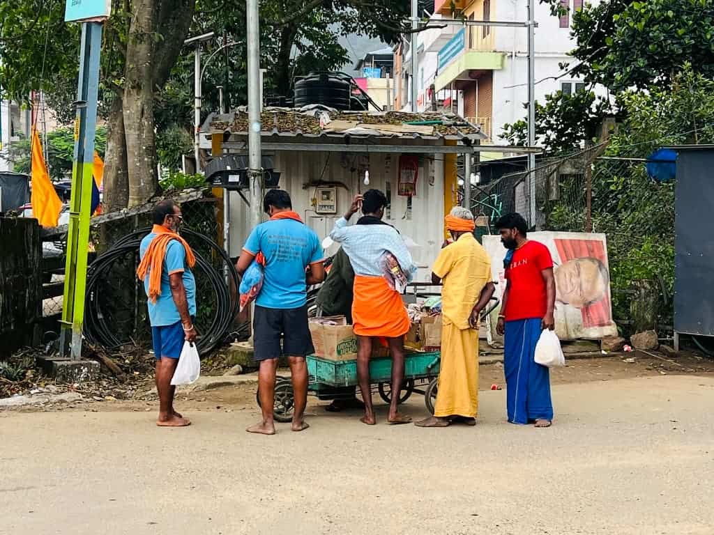 A group of men wearing brightly coloured clothing standing around a stall in Thekkady centre, Kerala