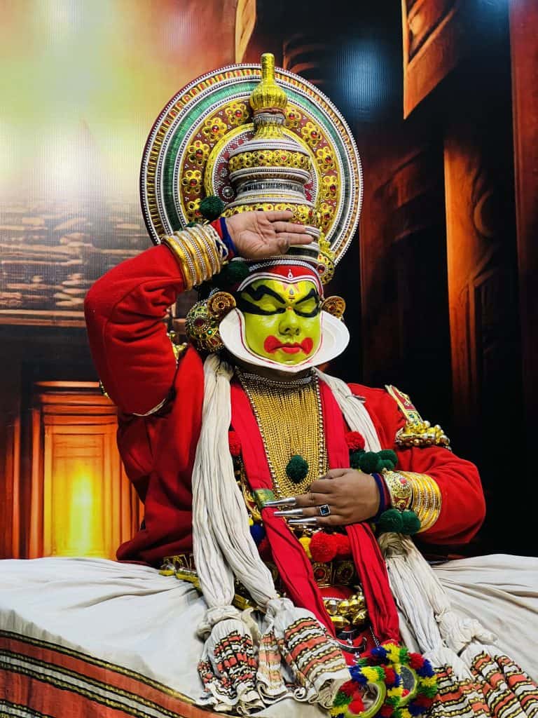 A Kathakali dancer dressed as Lord Krishna in a red costume and green painted face and gold jewellery. The Kathakali show at the Mudra Cultural Centre in Thekkady, Kerala.