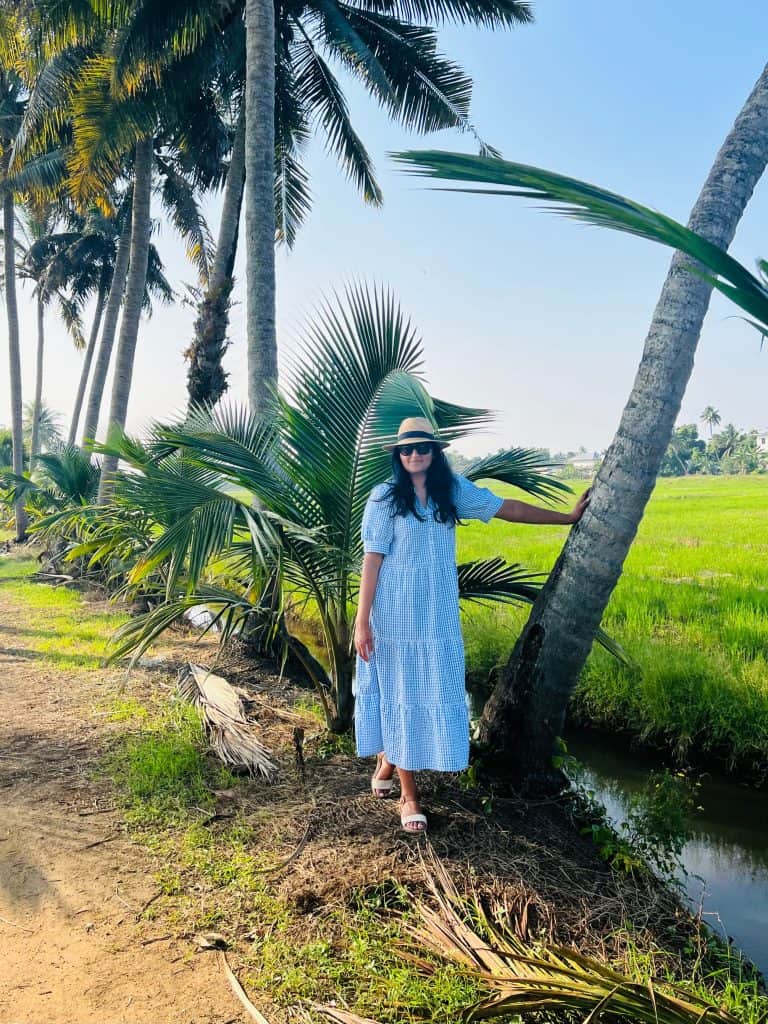 Beautiful Kerala backwaters: Bejal standing with hand on palm tree wearing a blue checked dress on the small waterways
