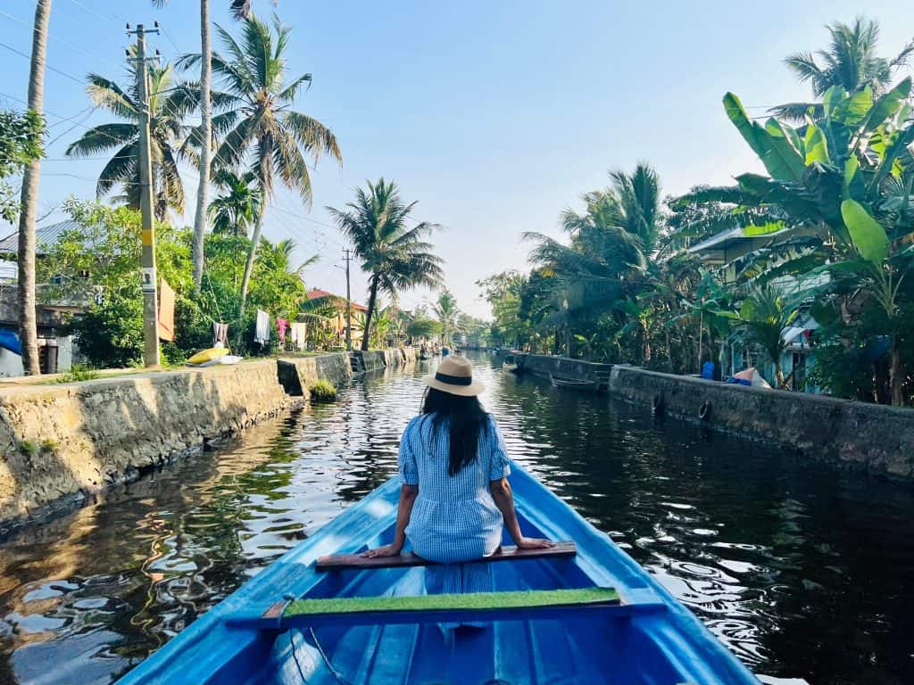 Beautiful Kerala backwaters: Bejal sitting at the front of a small fishing boat gliding through the canals surrounded by villages and locals on the banks.