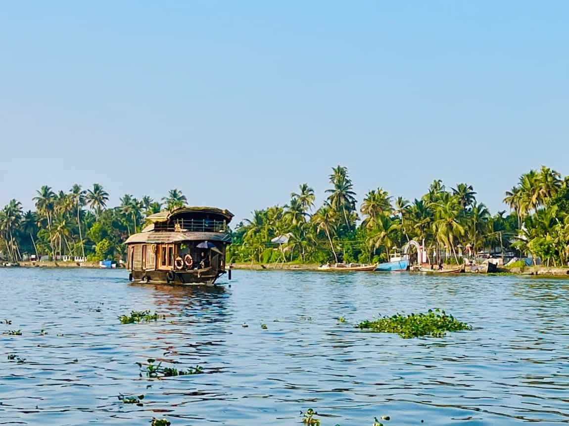 A traditional houseboat cruising down the larger waterways with palm trees in the background