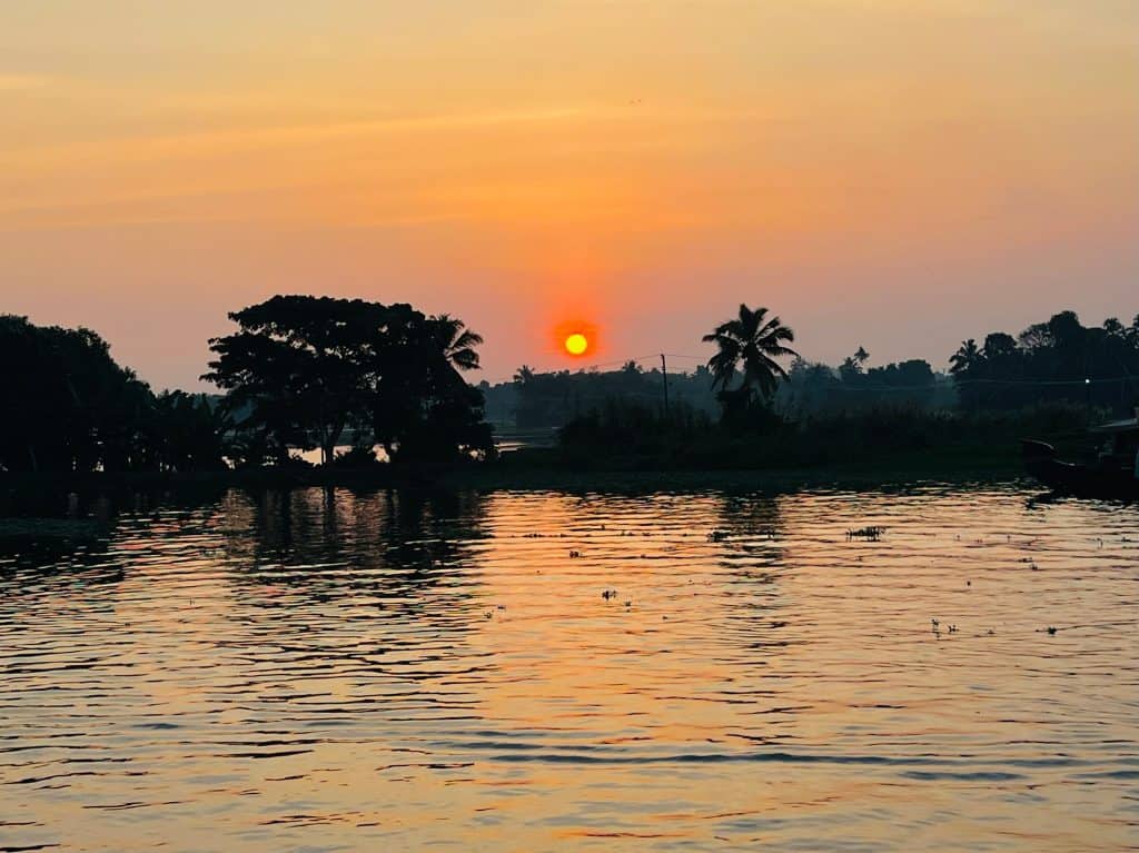 Beautiful Kerala backwaters: Sunset scenes over the waterways with palm trees in the background. A deep orange colour fills the sky