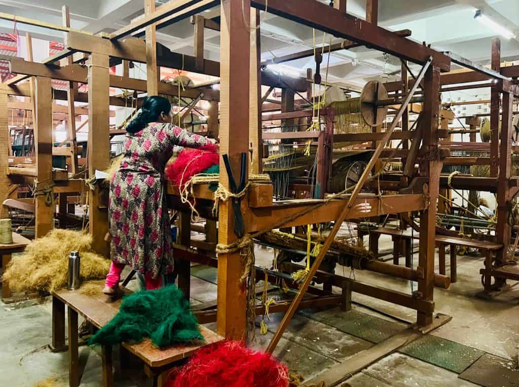 Lady weaving rugs from coloured coir using a traditional machine at the International Coir Museum