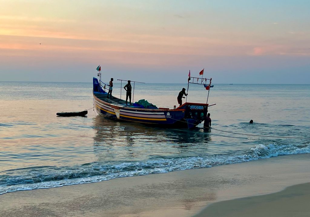 Fishermen on fishing boat coming into the shores of Marari Beach during sunset time