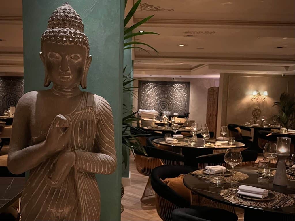 Indian Fine Dining At Varanasi. A tall buddha statue with a view of the rest of teh restaurant to the right hand side.