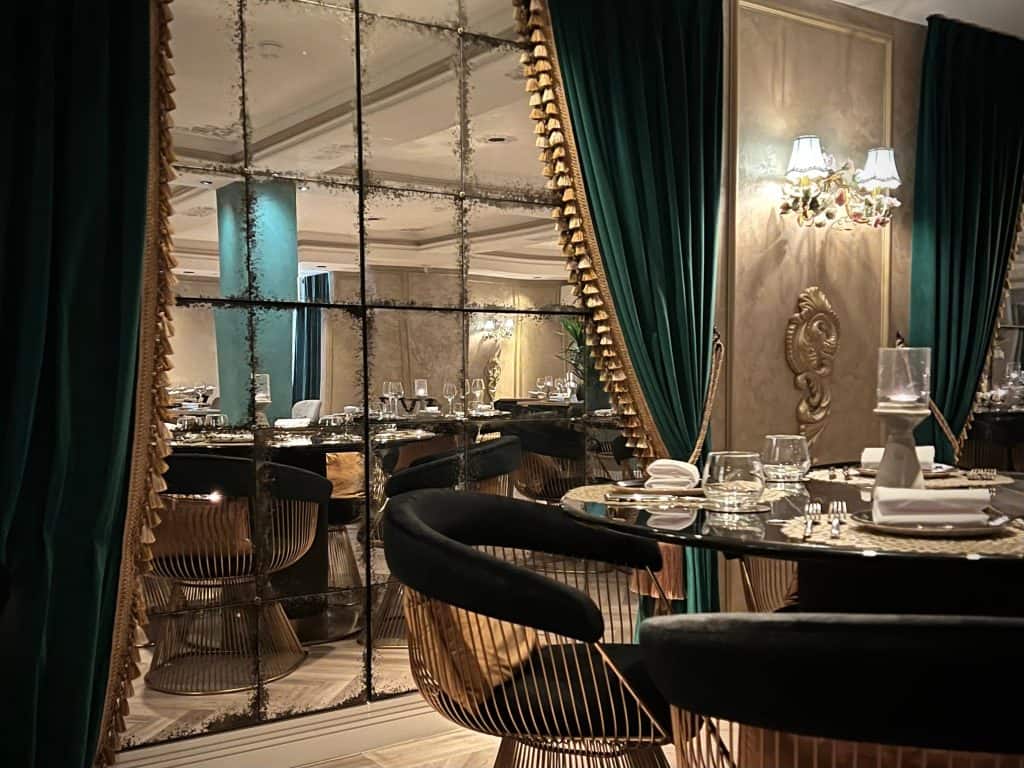 The mirror window interiors draped with teal velvet curtains and a set table in front at Varanasi, Leicester.