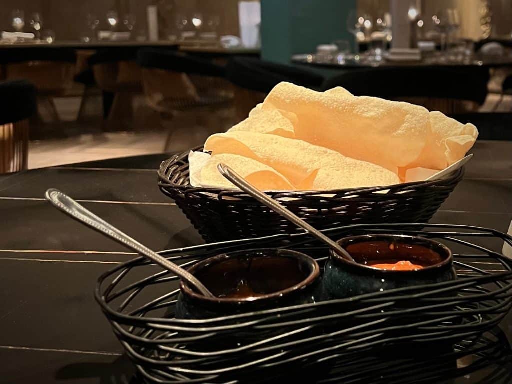 Poppodams in a black basket with mint and mango chutneys in a wire black bowl at Varanasi, Leicester